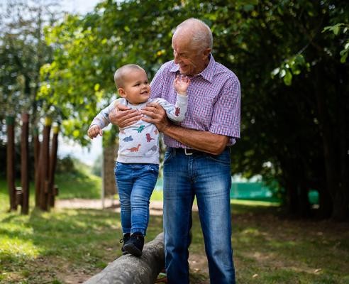 Opa mit Enkelkind, das auf Baumstamm balanciert 