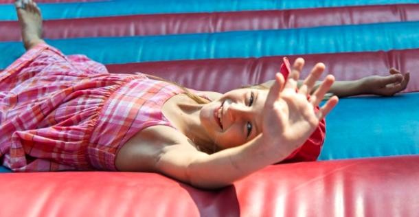 Titelfoto des Ferienpassprogramms 2020: Ein Mädchen liegt lachend auf einer Hüpfburg. 