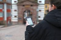 Frau hält Handy mit der "MeinHeidelberg"- App in der Hand