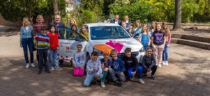 Die Medienpädagogin steht mit Kindern um das Elektrofahrzeug der Stadtbücherei
