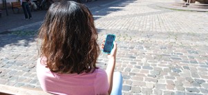Eine Frau sitzt auf einer Bank und schaut in ein Smartphone, das sie in ihren Händen hält