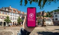 Hochgehaltenes Handy mit der App vor dem Marktplatz