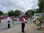 Scheidsrichter beobachten zwei Feuerwehrangehörige beim Aufbau eines Gerätes