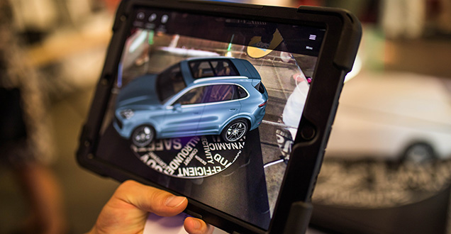 Eine Hand hält ein Tablet, in dem ein animiertes Auto angezeigt wird (Foto: Dittmer)
