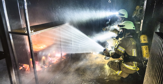 Flammenschein über dem Helm eines Feuerwehrmanns bei einer Übung