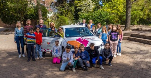 Die Medienpädagogin steht mit Kindern um das Elektrofahrzeug der Stadtbücherei