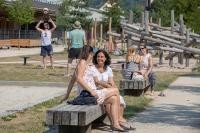 Zwei Frauen sitzen auf einer Bank und unterhalten sich. Im Hintergrund ist ein Spielplatz auf dem weitere Personen sind (Foto: Buck)