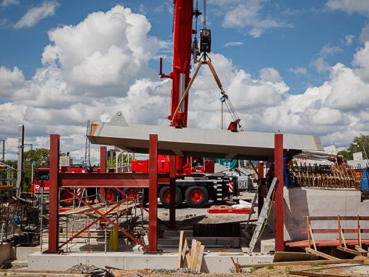 16. Mai 2024: Ein großer Autokran hebt das erste Brückenelement der Brücke ein. An einem Kran hängt ein stählernes Element einer Brücke