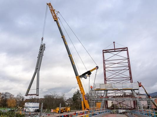 26. November 2024: Der insgesamt 112 Tonnen schwere Pylon aufgestellt und montiert. (Foto: Buck) Ein stählernes Bauteil hängt von einem großen Kran.