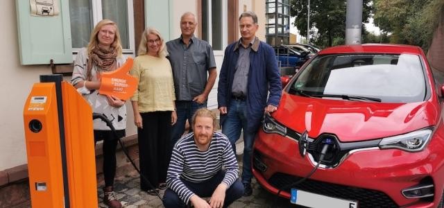 Fünf Personen zwischen neuer E-Ladesäule und E-Auto, welches geladen wird.