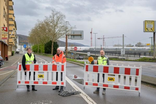 Erste Sperrungen an der Baustelle der Montpellierbrücke entfernt: Erster Bürgermeister Jürgen Odszuck (von links), Klaus-Peter Hofbauer und Bülent Kardogan vom Tiefbauamt öffneten am Mittwoch, 25. März 2026, die Durchfahrt in einem Abschnitt der Lessingstraße wieder für den Verkehr. (Foto: Philipp Rothe) Drei Personen, die ein Absperrung auf einer Straßen abbauen.