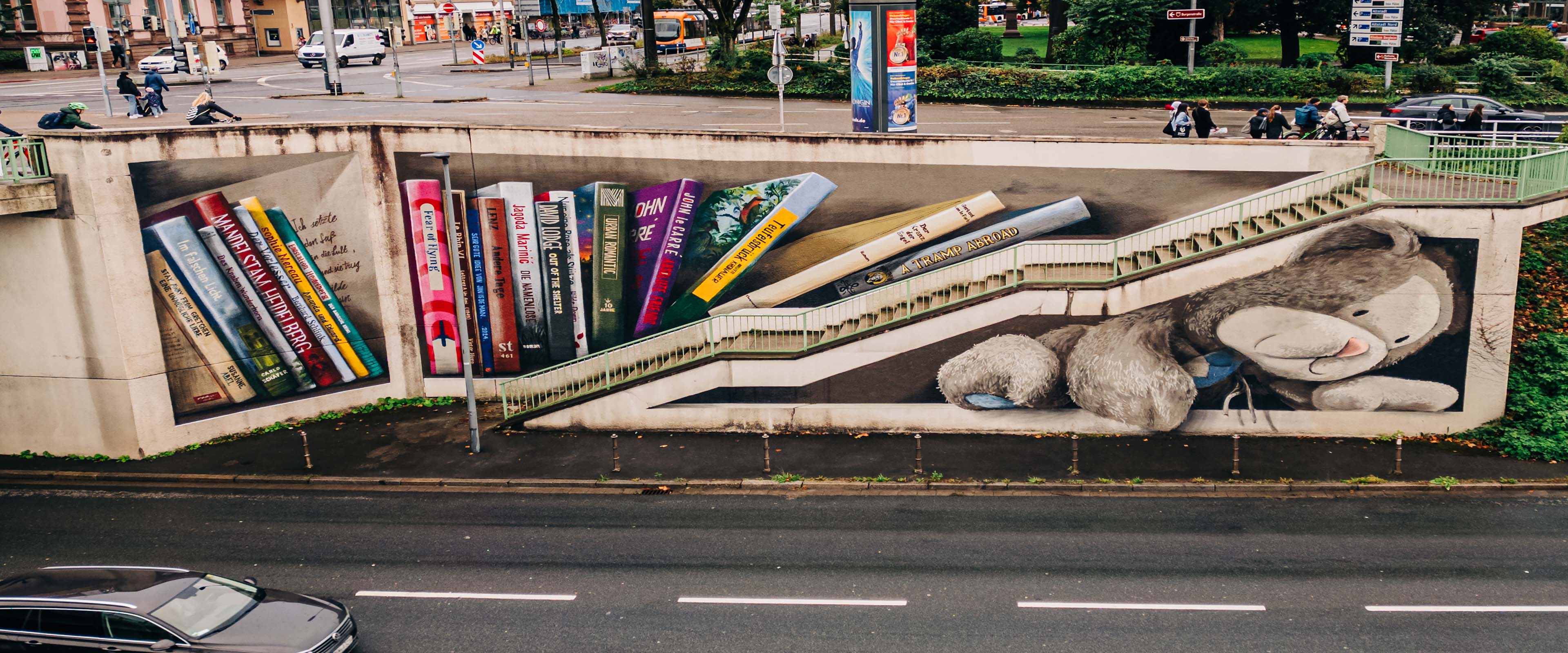 Wandgemälde von JanIsDeMan an der Theodor-Heuss-Brücke mit Büchern und einem Kuscheltier 