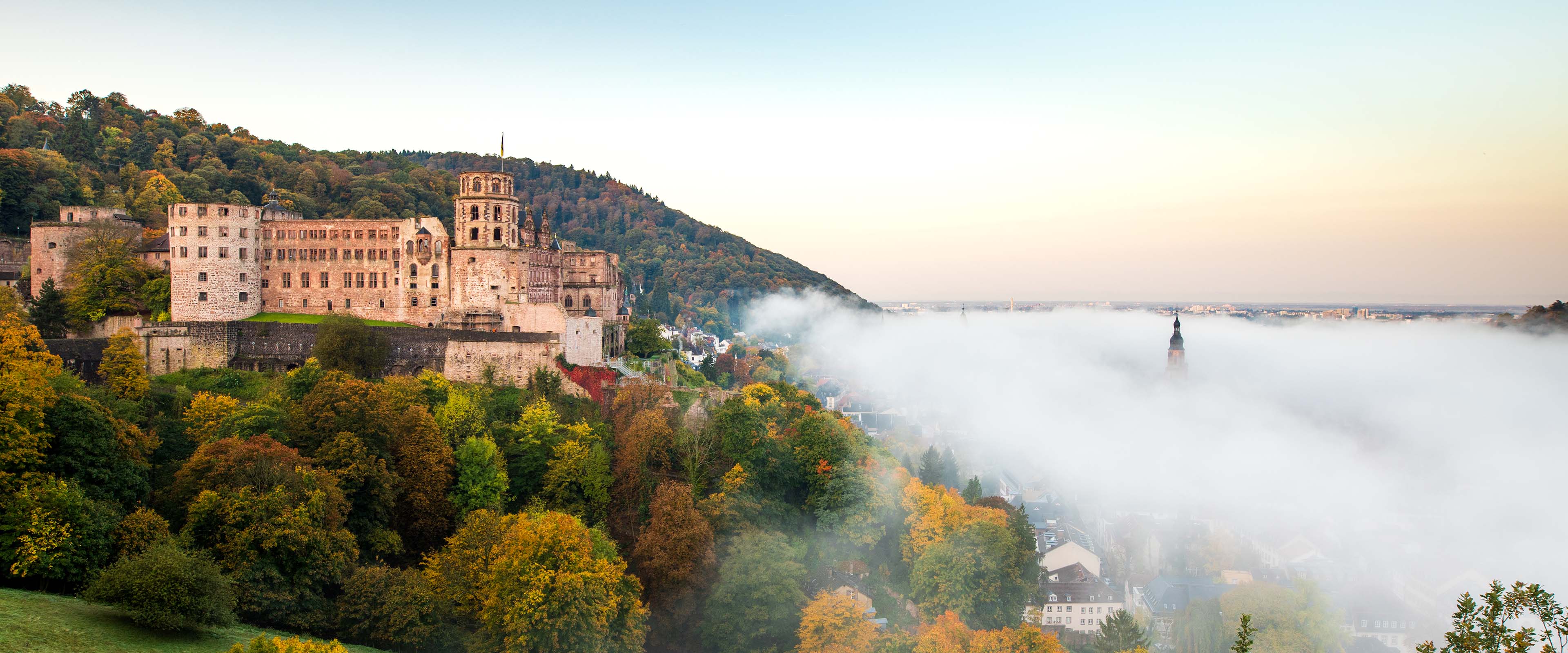 Heidelberger Sandstein-Schloss hinter Bäumen mit Herbstlaub und blauem Himmel