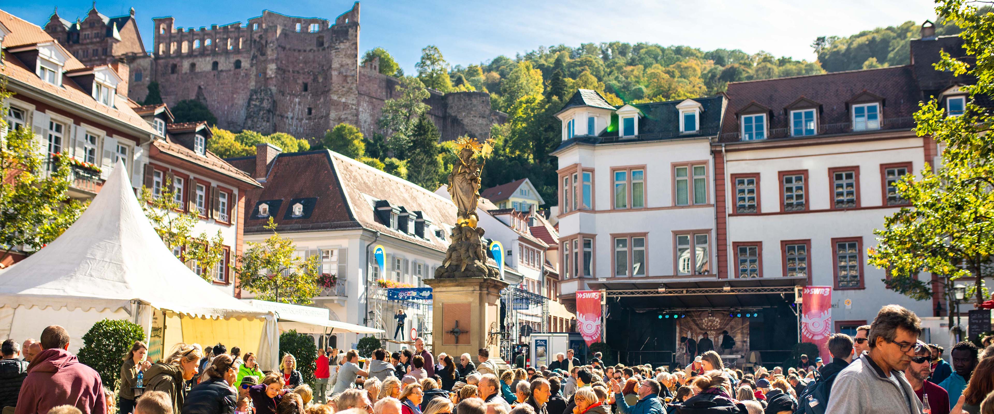 Menschen auf Altstadt-Platz in Heidelberg mit Blick aufs Heidelberger Schloss