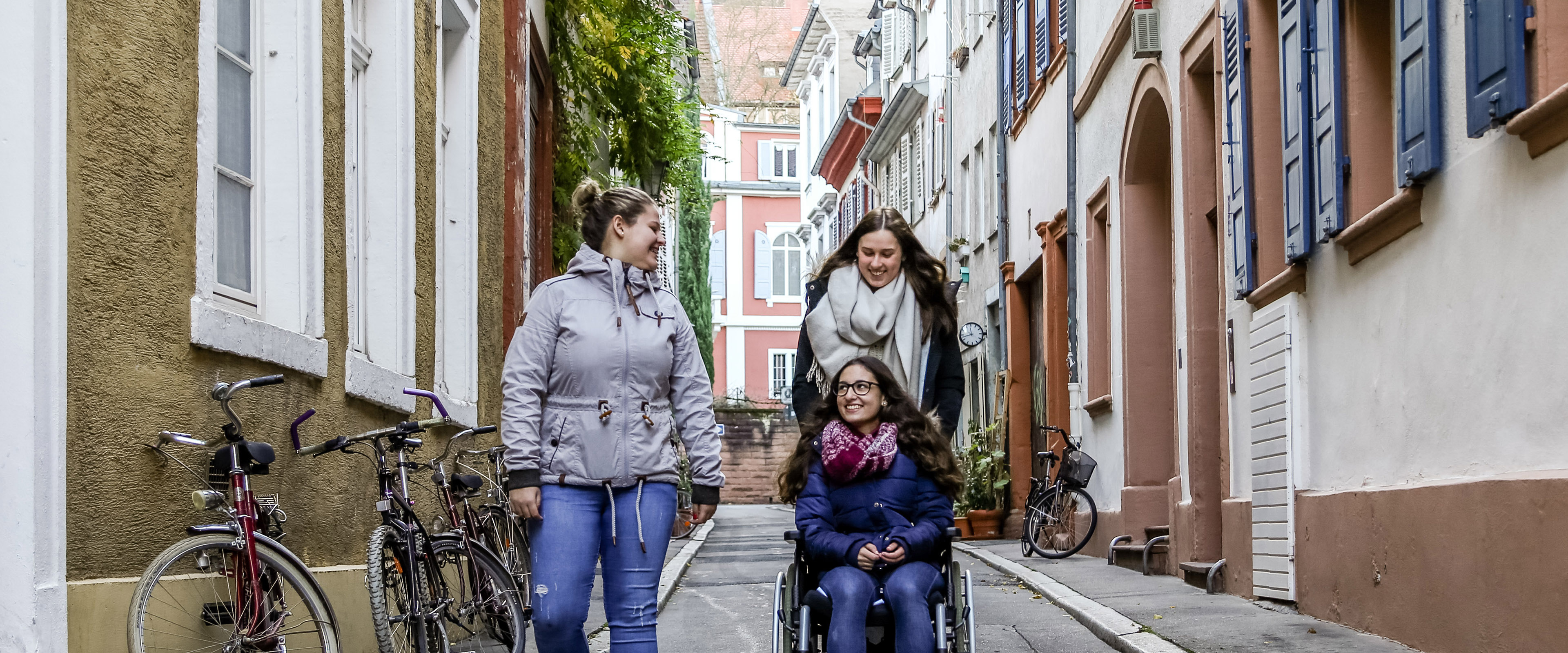 Drei Frauen, eine im Rollstuhl, in einer Altstadtgasse