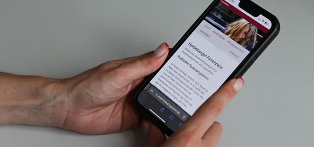 Hand hält Smartphone auf der die Ferienpass-Webseite geöffnet ist