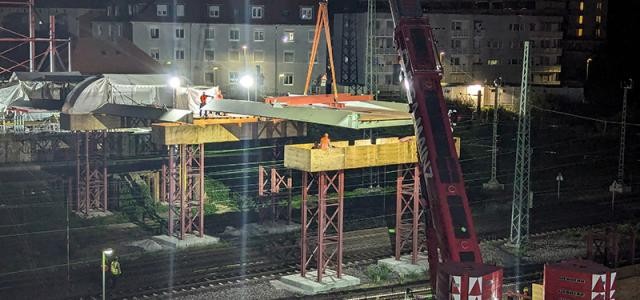 Kran hebt Platte auf zwei Stützpfosten über Schienen bei Nacht