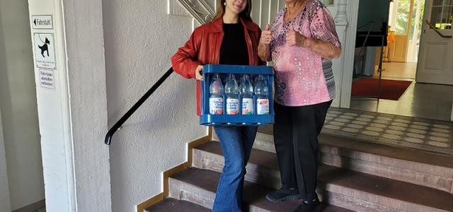 Junge Frau trägt alter Frau einen Kasten Wasser in die Wohnung