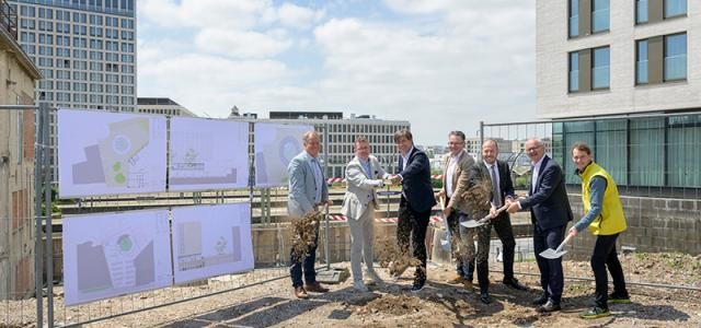 Gruppe von Männern schaufeln Sand. Im Hintergrund sind die neuen Hotels am Bahnhof zu sehen