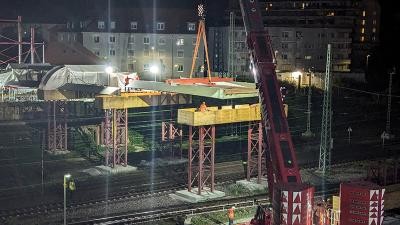 Kran hebt Platte auf zwei Stützpfosten über Schienen bei Nacht