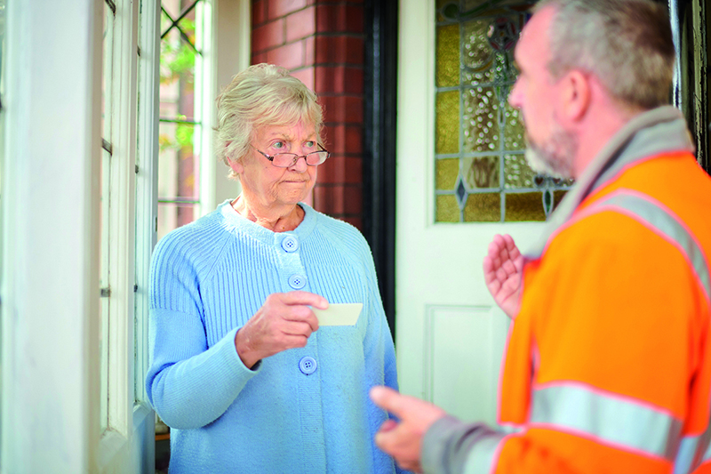 Ältere Dame an Wohnungstür spricht mit Mann in orangefarbener Arbeitskleidung