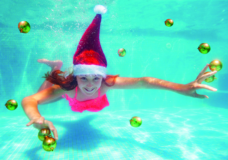 Mädchen mit Weihnachtsmannmütze schwimmt in Becken mit Christbaumkugeln