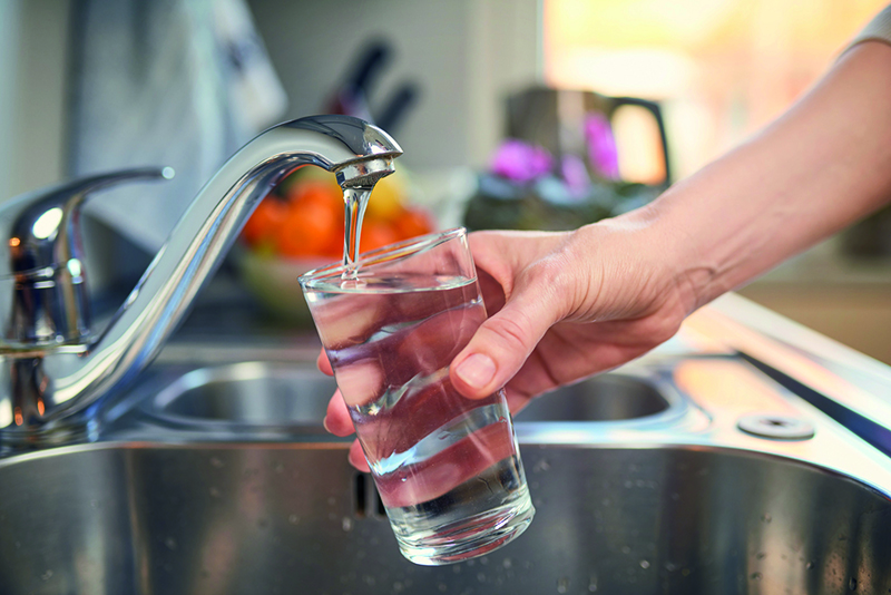 Wasserhahn mit gefülltem Glas und Hand